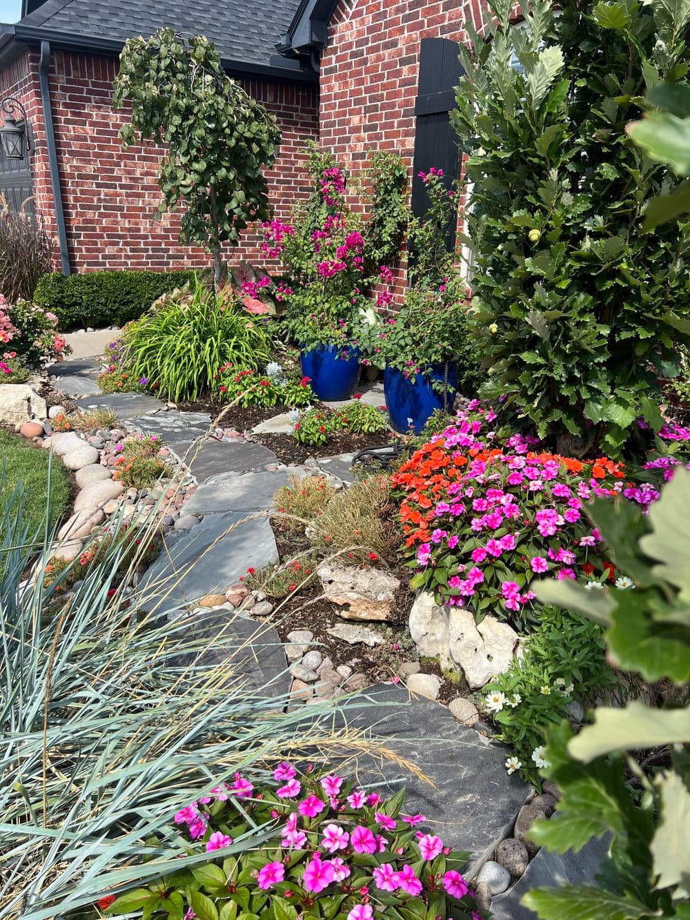 Lush garden pathway lined with colorful flowers and blue pots, showcasing vibrant landscaping.