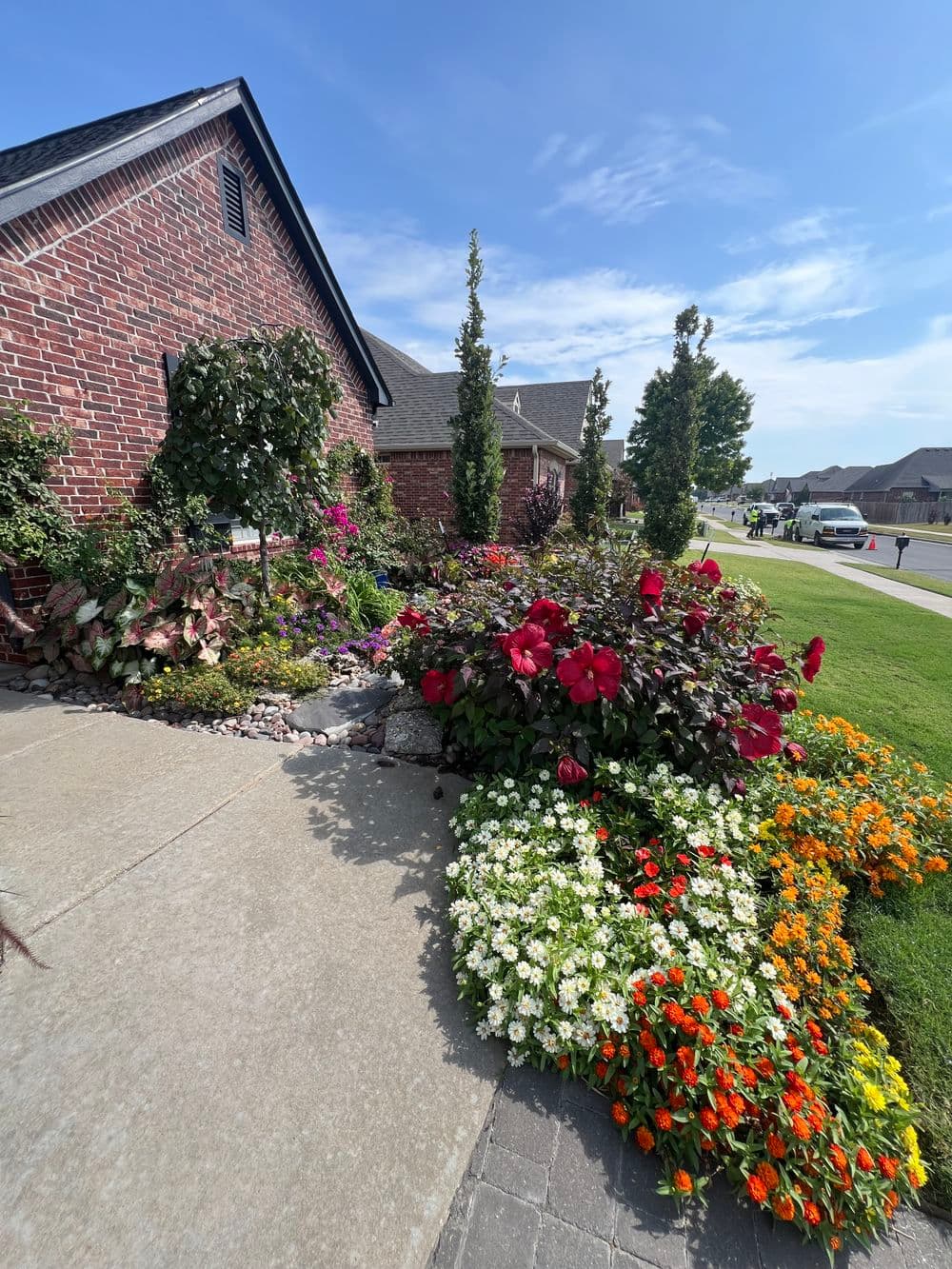Vibrant flower garden with colorful blooms and brick home entrance on a sunny day.