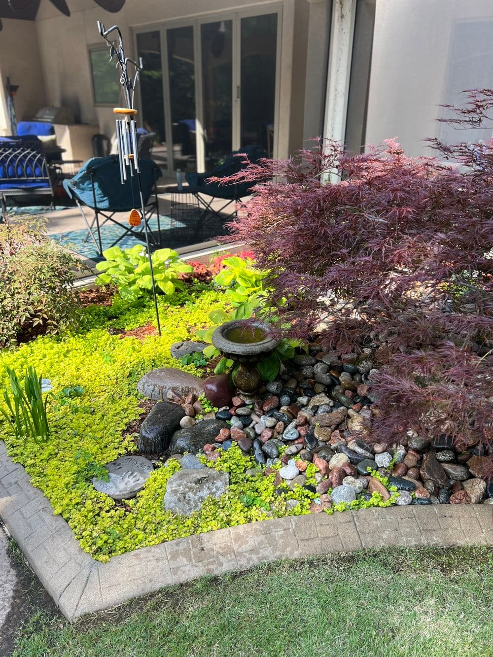 Lush garden landscape with colorful stones, water feature, and vibrant greenery.