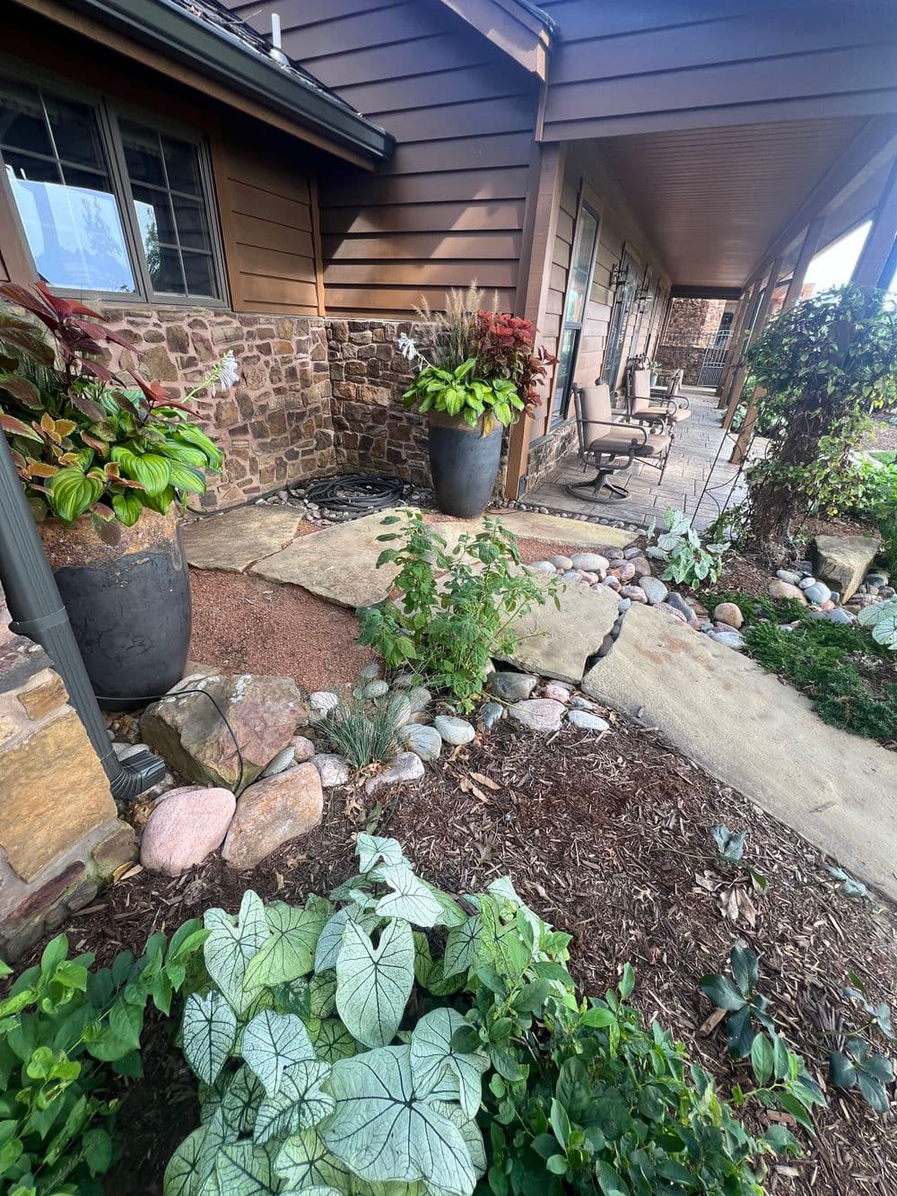 Lush garden pathway with potted plants alongside a stone porch and seating area.