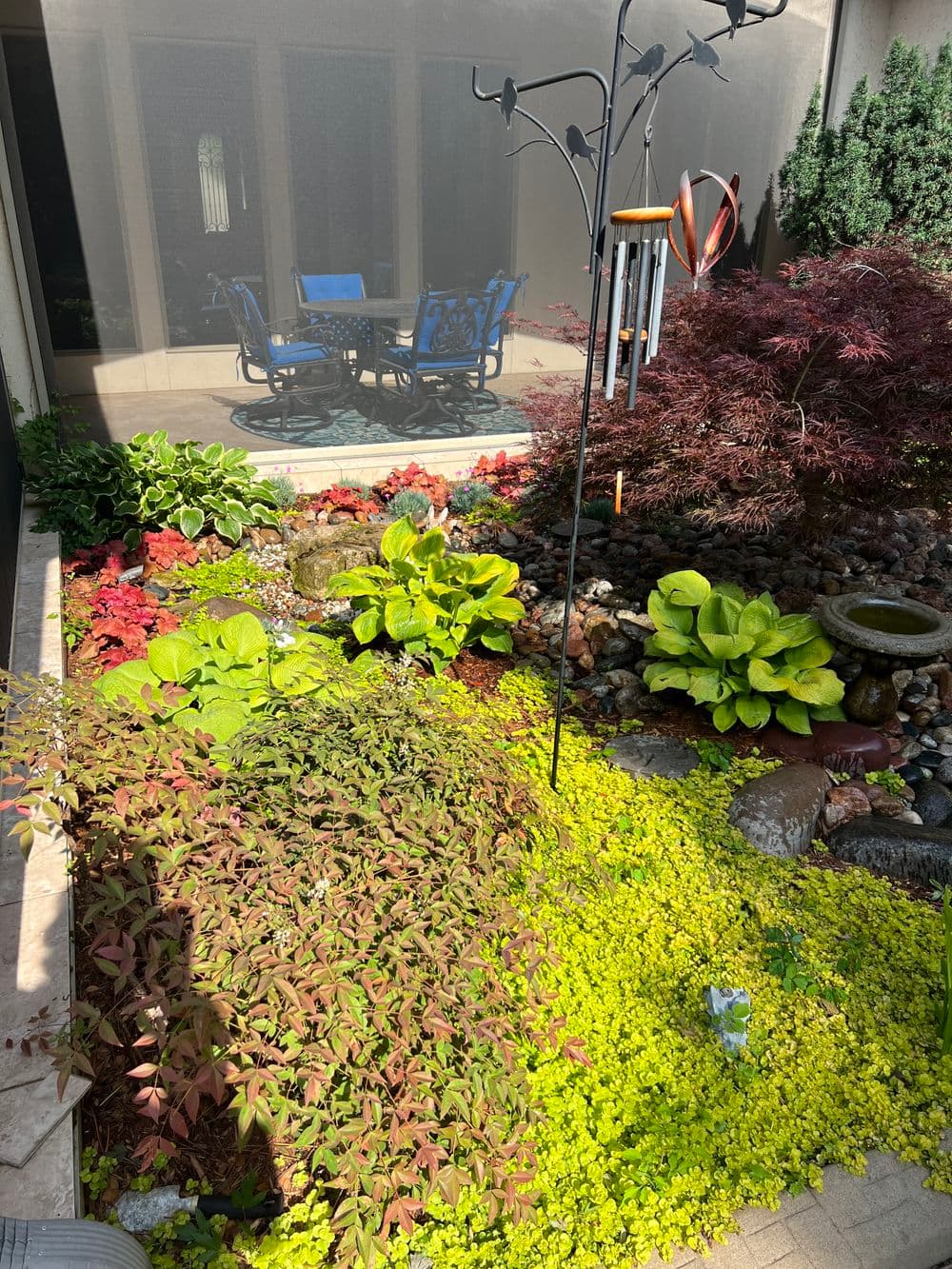 Vibrant garden with colorful plants, decorative wind chime, and patio seating in background.